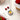 Necklace with a smiley face charm and red gemstones on a white surface with strawberries.