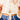 Gold necklace with a pendant held by a person wearing a white sweater and blue jeans.
